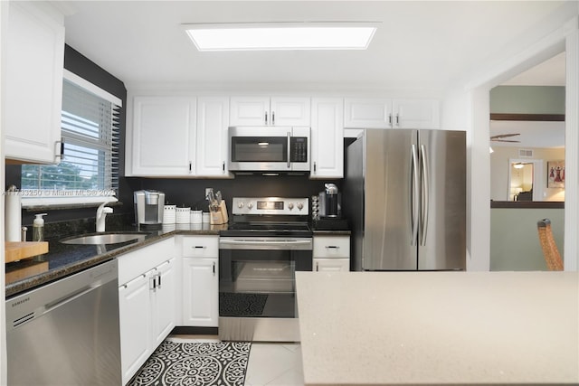 kitchen with white cabinetry, stainless steel appliances, light tile patterned flooring, and dark stone counters