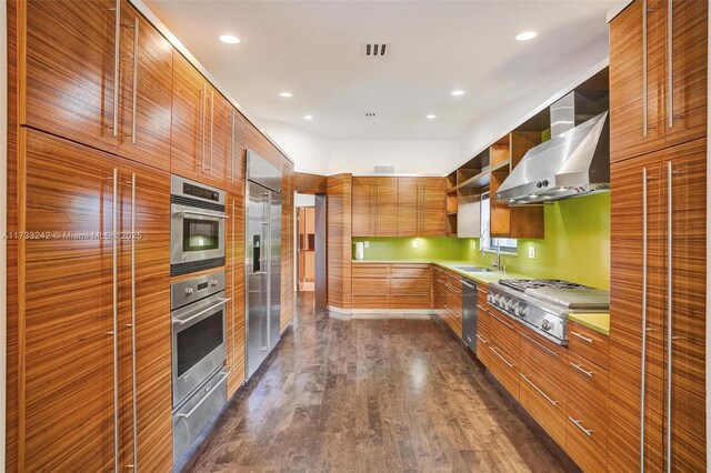 kitchen with dark wood-type flooring, appliances with stainless steel finishes, wall chimney exhaust hood, and sink