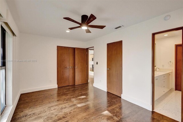 unfurnished bedroom with sink, ensuite bath, dark hardwood / wood-style floors, and multiple closets