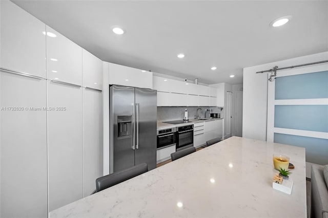 kitchen with sink, white cabinetry, appliances with stainless steel finishes, a barn door, and light stone countertops