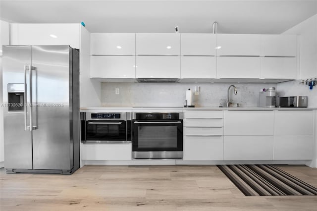 kitchen featuring sink, appliances with stainless steel finishes, range hood, decorative backsplash, and white cabinets