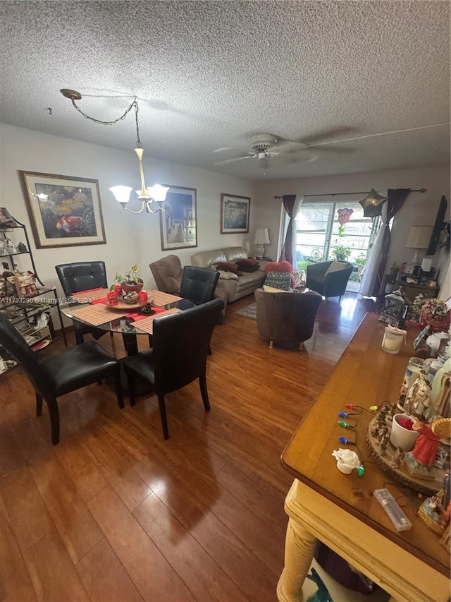 dining room with ceiling fan with notable chandelier, wood-type flooring, and a textured ceiling