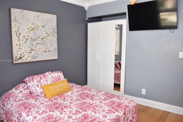 bedroom with hardwood / wood-style flooring, ornamental molding, and a closet