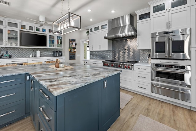 kitchen with blue cabinets, a warming drawer, stainless steel appliances, wall chimney exhaust hood, and visible vents