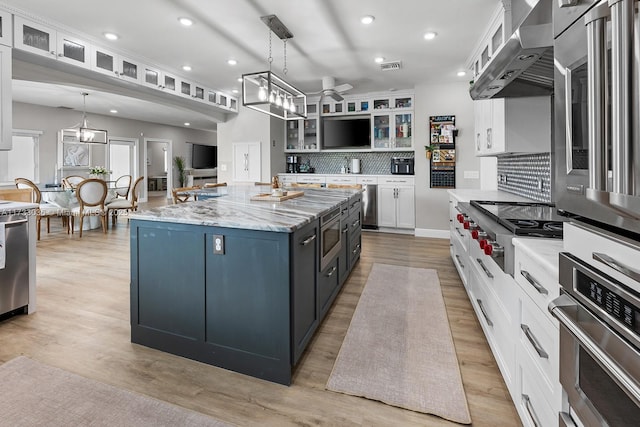kitchen featuring wall chimney range hood, tasteful backsplash, ceiling fan, white cabinets, and appliances with stainless steel finishes