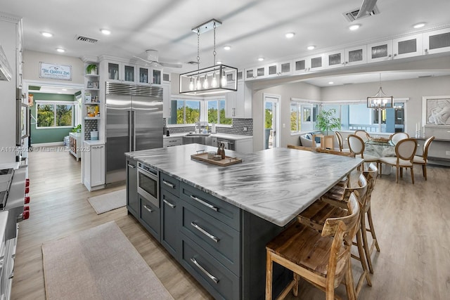 kitchen featuring a sink, built in appliances, light wood finished floors, white cabinets, and visible vents