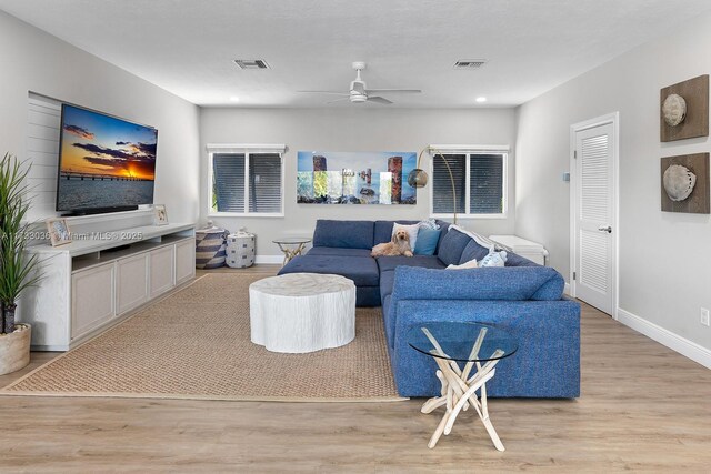 living room with baseboards, a ceiling fan, visible vents, and light wood-type flooring
