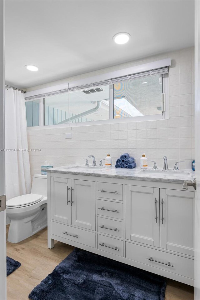 full bathroom featuring toilet, wood finished floors, a sink, and double vanity