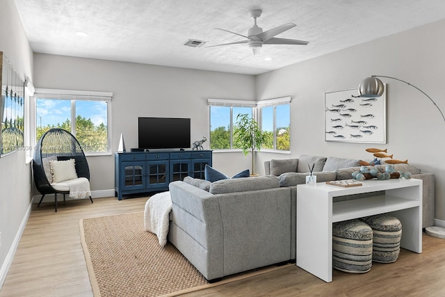 living room featuring ceiling fan, light wood-type flooring, visible vents, and plenty of natural light