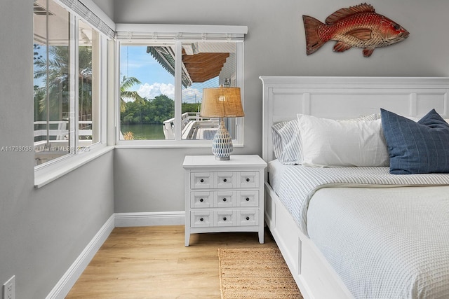 bedroom with baseboards, light wood-style floors, and a water view