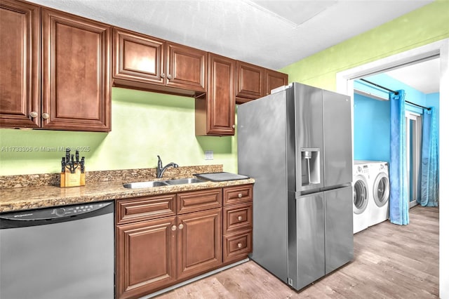 kitchen with sink, light stone counters, separate washer and dryer, light wood-type flooring, and appliances with stainless steel finishes