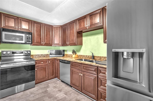 kitchen with sink, light stone counters, a textured ceiling, light wood-type flooring, and appliances with stainless steel finishes