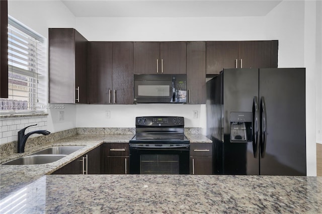 kitchen with light stone countertops, sink, dark brown cabinets, and black appliances