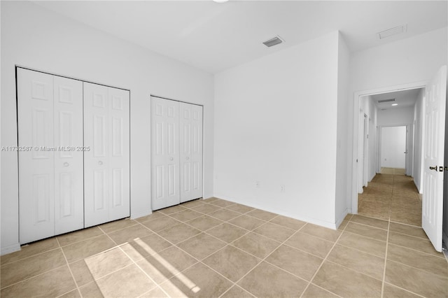 unfurnished bedroom with light tile patterned flooring and two closets