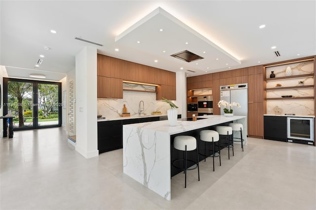 kitchen featuring sink, refrigerator, a large island with sink, a kitchen breakfast bar, and light stone countertops