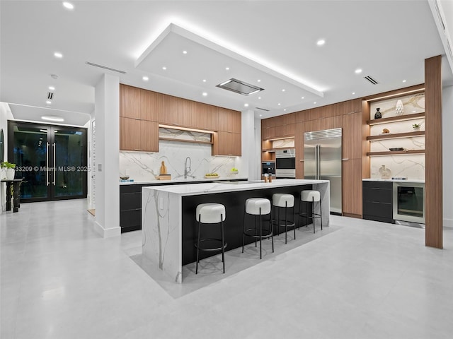 kitchen featuring wine cooler, sink, a large island with sink, appliances with stainless steel finishes, and a kitchen breakfast bar