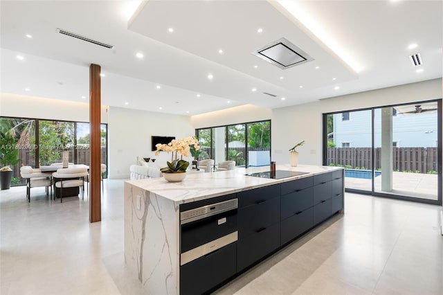 kitchen with a spacious island, light stone counters, a raised ceiling, black electric stovetop, and oven