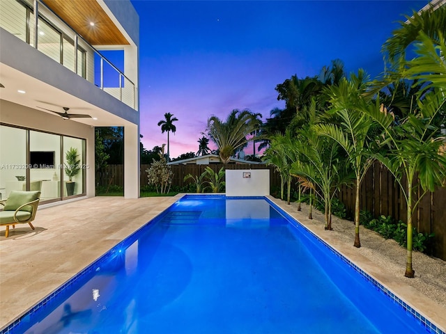 pool at dusk featuring ceiling fan and a patio