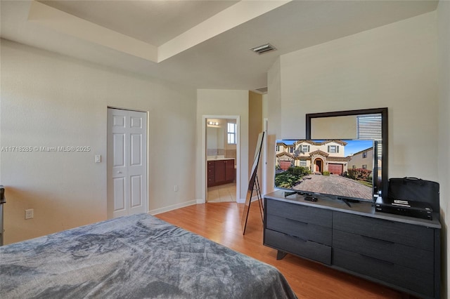 bedroom featuring ensuite bathroom, a raised ceiling, and light hardwood / wood-style flooring