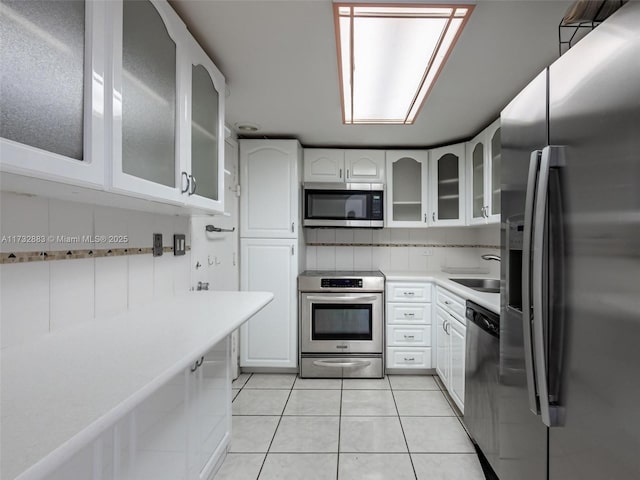 kitchen featuring stainless steel appliances, light tile patterned flooring, sink, and white cabinetry