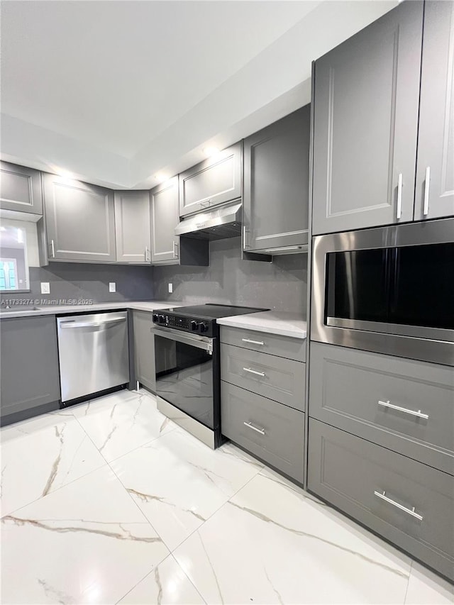kitchen featuring marble finish floor, stainless steel appliances, light countertops, range hood, and gray cabinetry