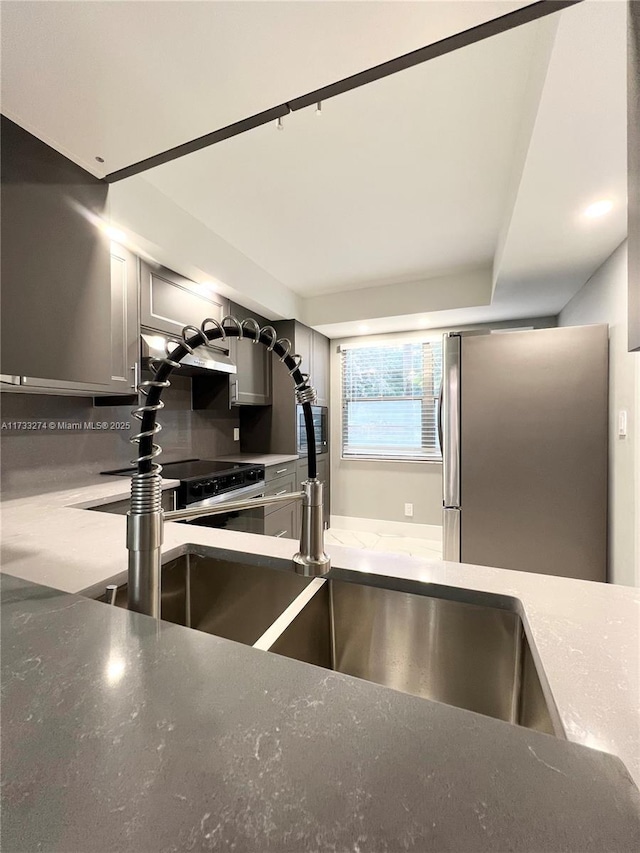 kitchen with tasteful backsplash, sink, gray cabinetry, and stainless steel refrigerator