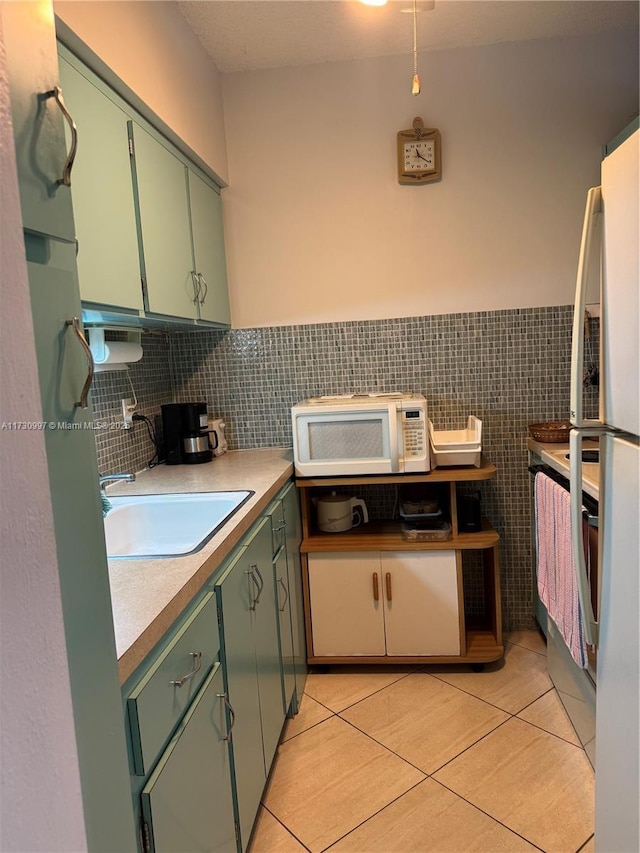 kitchen featuring sink, tile walls, light tile patterned floors, fridge, and green cabinets