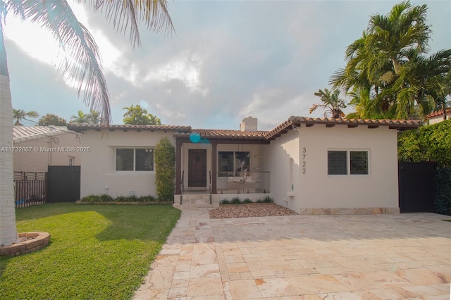 mediterranean / spanish home featuring fence, a chimney, a front lawn, and stucco siding