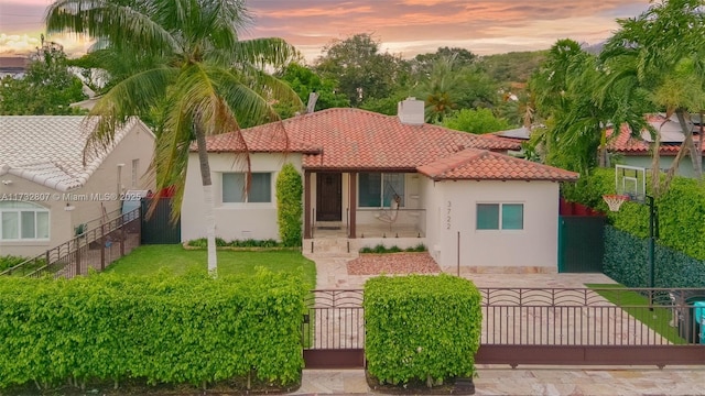 mediterranean / spanish-style home featuring a fenced front yard, a tiled roof, a gate, stucco siding, and a chimney