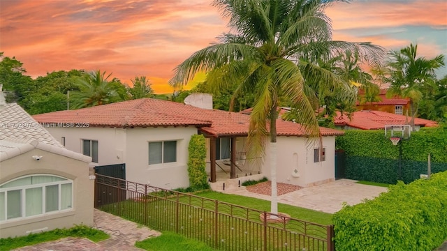 back of house at dusk with a fenced front yard, a lawn, a tiled roof, and stucco siding