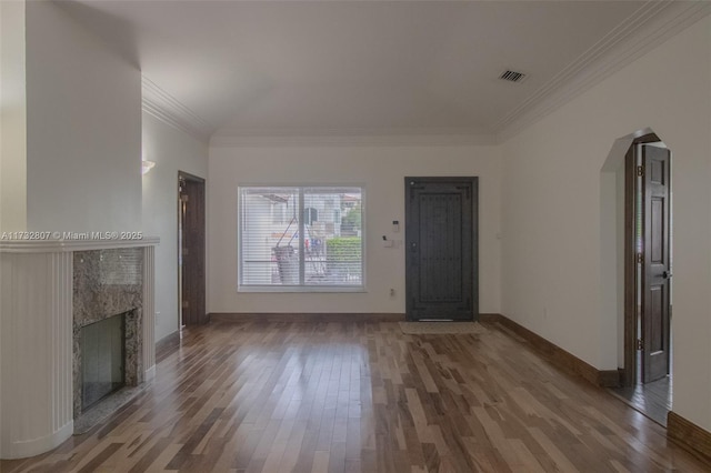 unfurnished living room featuring arched walkways, visible vents, a premium fireplace, ornamental molding, and wood finished floors