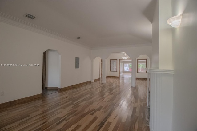 unfurnished living room with arched walkways, crown molding, visible vents, wood finished floors, and electric panel