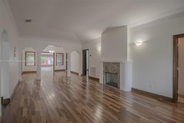 unfurnished living room featuring visible vents, a premium fireplace, arched walkways, and wood finished floors