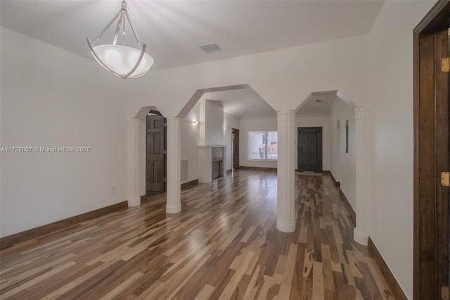 unfurnished living room featuring arched walkways, dark wood-style flooring, a fireplace, ornate columns, and baseboards