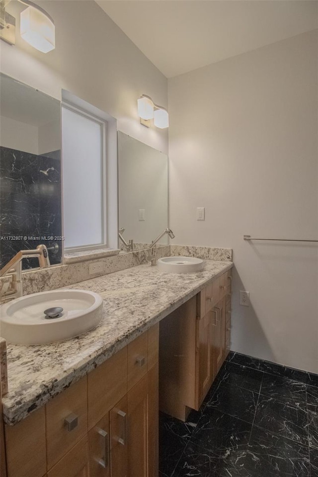 full bath with marble finish floor, double vanity, and a sink