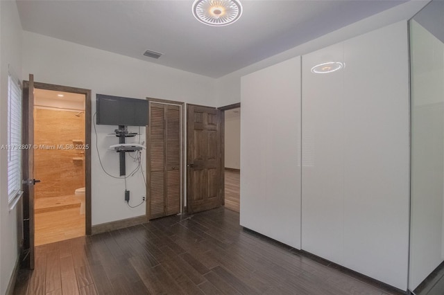 unfurnished bedroom featuring dark wood-style flooring, visible vents, and ensuite bath