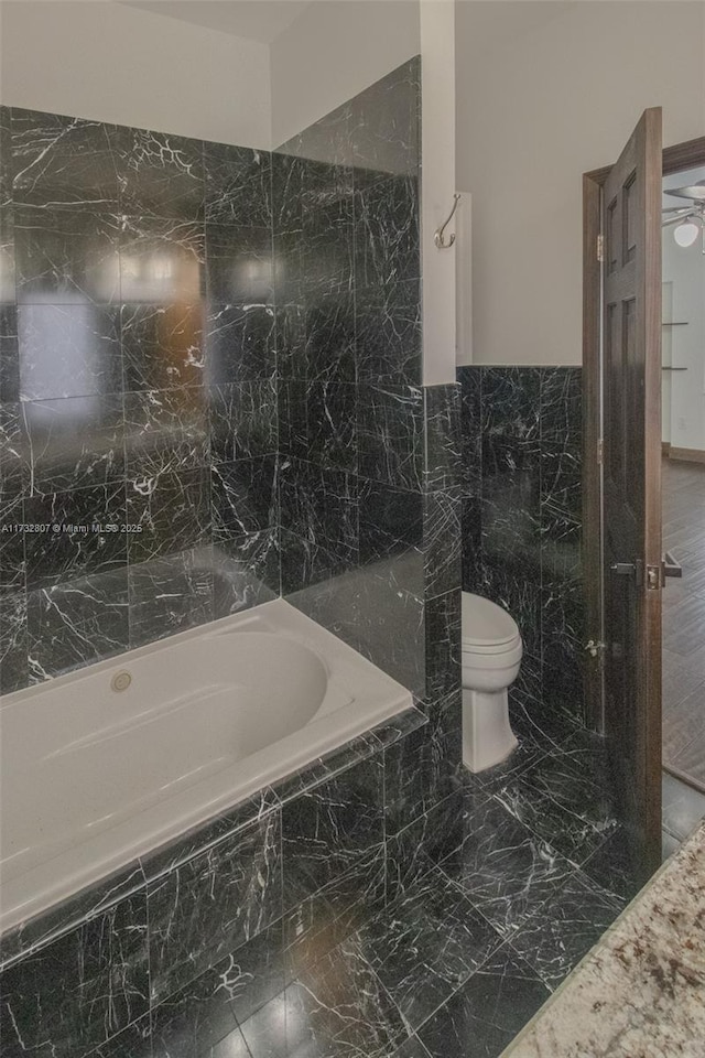 bathroom featuring toilet, tiled bath, and tile walls