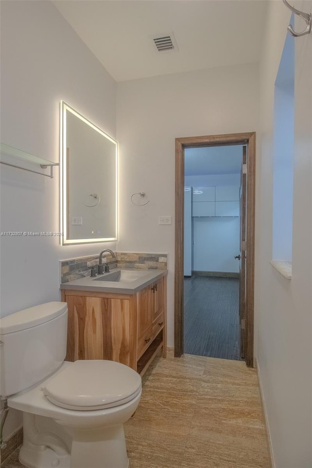 half bath with baseboards, visible vents, vanity, and toilet