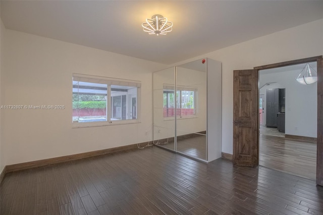 unfurnished bedroom with a closet, multiple windows, baseboards, and dark wood-style flooring