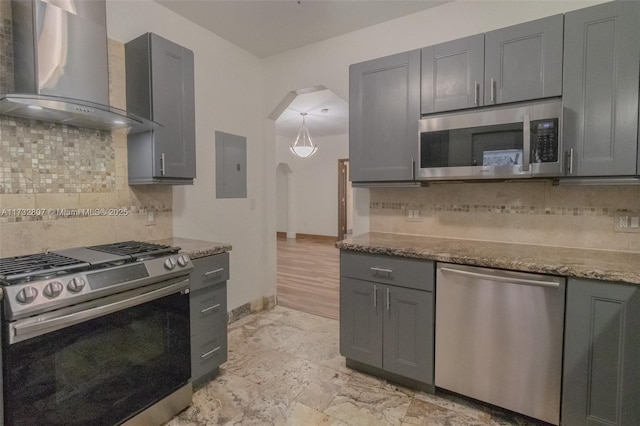 kitchen featuring arched walkways, appliances with stainless steel finishes, dark stone countertops, electric panel, and wall chimney exhaust hood