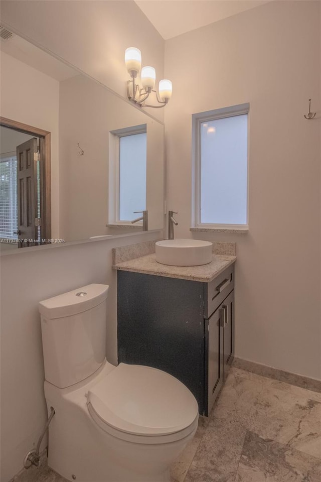 half bathroom featuring a chandelier, baseboards, vanity, and toilet