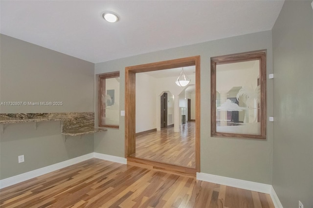 spare room featuring arched walkways, baseboards, and wood finished floors