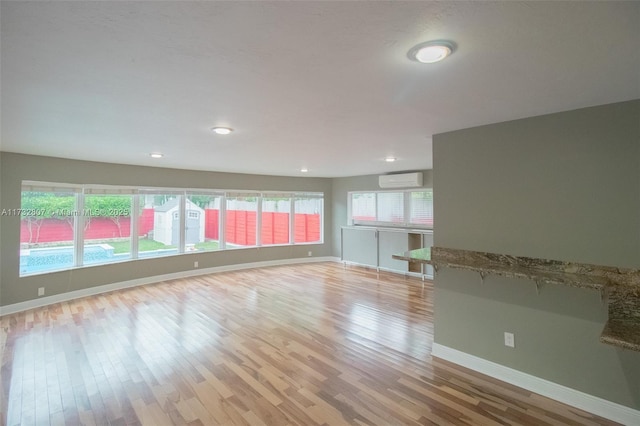 empty room with plenty of natural light, a wall unit AC, light wood-style flooring, and baseboards