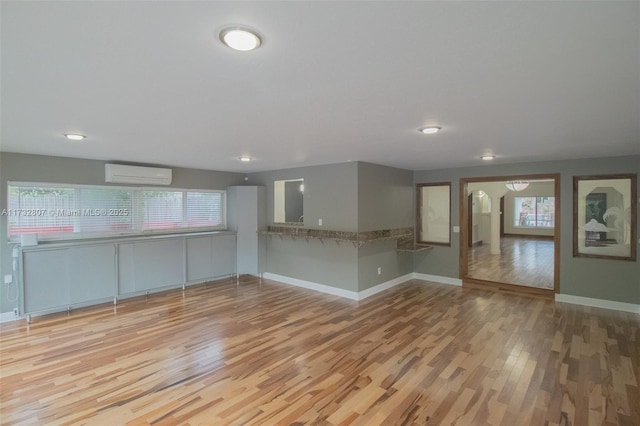 unfurnished room featuring light wood-style floors, a wall unit AC, and baseboards