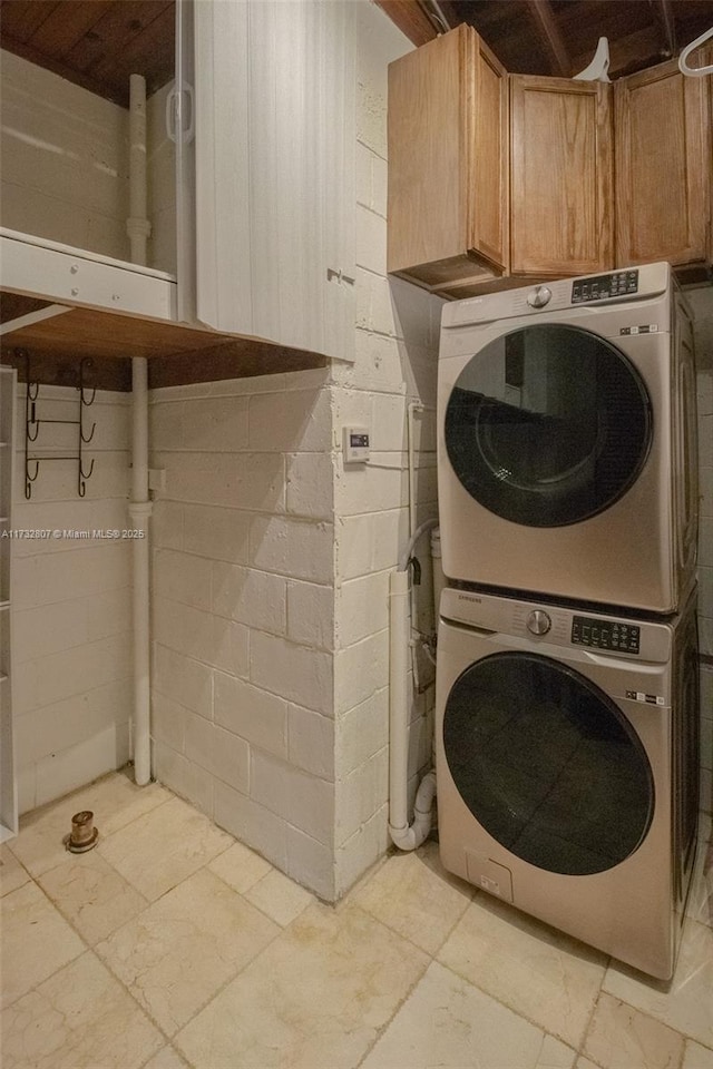 clothes washing area featuring stacked washing maching and dryer, cabinet space, and stone tile floors