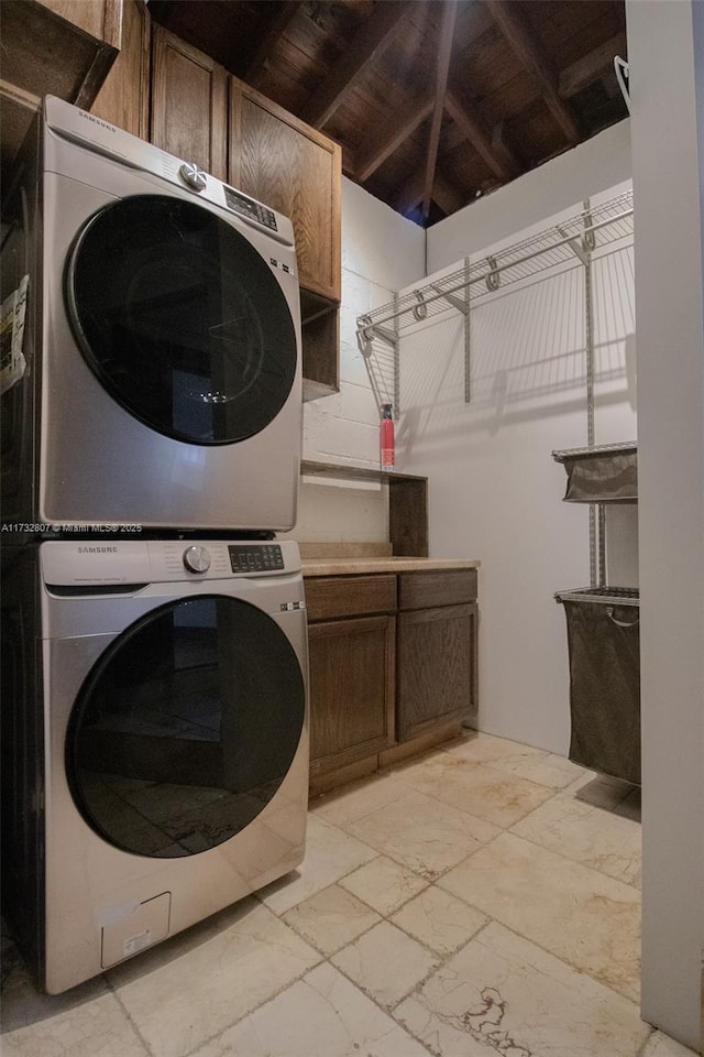 laundry room with stacked washer / drying machine, cabinet space, and stone tile floors