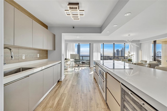 kitchen with wine cooler, sink, light wood-type flooring, black electric cooktop, and decorative backsplash