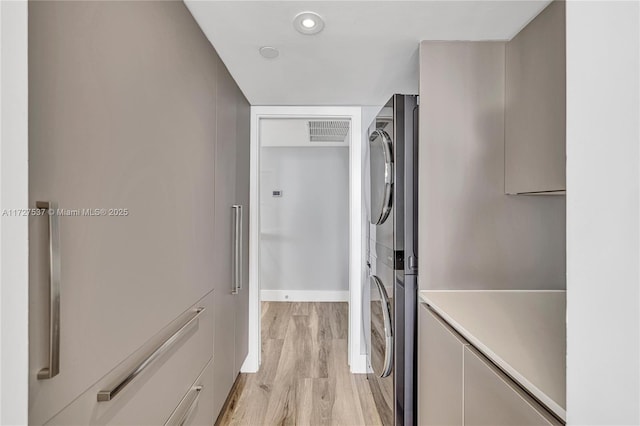 clothes washing area featuring stacked washing maching and dryer and light hardwood / wood-style floors