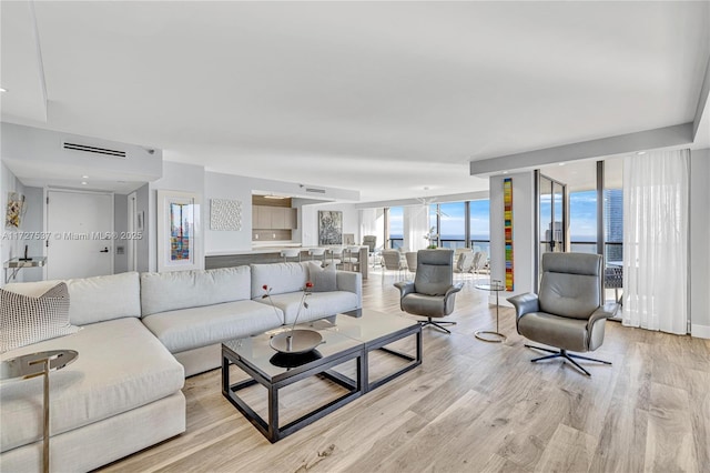 living room with expansive windows, a water view, and light hardwood / wood-style flooring