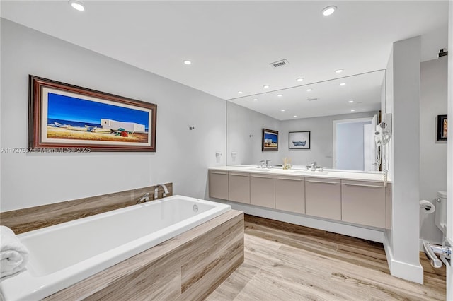 bathroom featuring a relaxing tiled tub, vanity, toilet, and hardwood / wood-style flooring